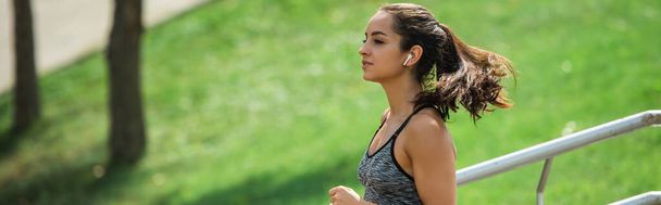donna sportiva in auricolari senza fili ascoltare musica mentre corre nel parco - Foto, immagini
