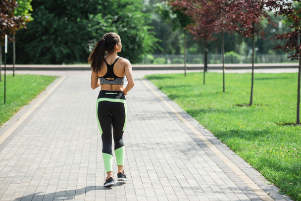 back view of sportive woman in wireless earphones listening music while running in park - Foto, Imagem