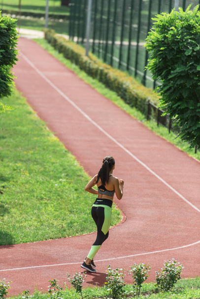 full length of sportive woman in crop top and leggings running on stadium - Φωτογραφία, εικόνα