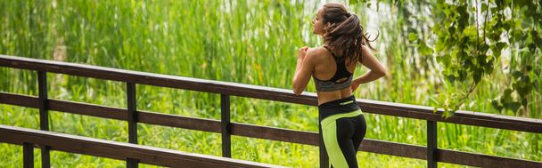 gelukkige sportvrouw in gewas top en leggings joggen op brug in park, banner - Foto, afbeelding