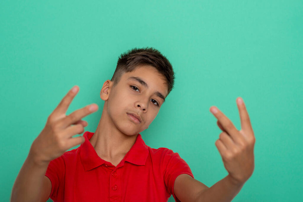 Studiotaille nach oben Porträt eines jungen ernsthaften Teenagers in rotem Hemd, der mit einem Friedens- oder Siegeszeichen vor grünem Hintergrund gestikuliert - Foto, Bild