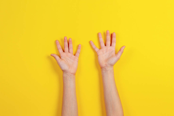 Two kid arms on yellow background. Top view to empty opened palms up. Hands gesture - Foto, Imagem