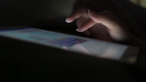 De vinger van een vrouw glijdt over het scherm van een tablet om sociale media af te spelen zonder het licht aan te zetten, in bed voordat ze in slaap valt. - Video