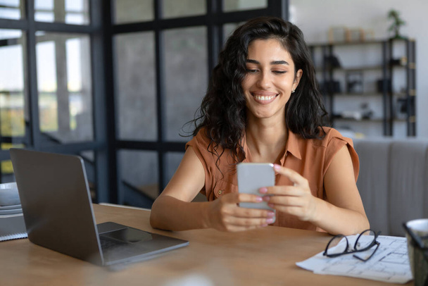 Ευτυχισμένη νεαρή Καυκάσια κυρία χρησιμοποιώντας smartphone και laptop για online εργασία στο σπίτι, αντιγραφή χώρου - Φωτογραφία, εικόνα