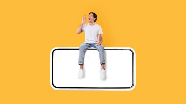Guy sitting on white empty smartphone screen and making announcement - Photo, Image