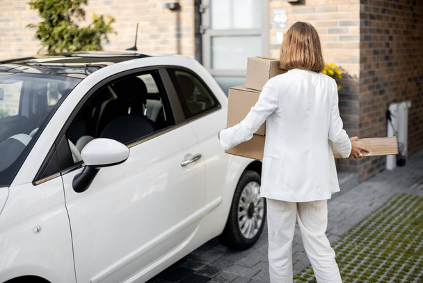 Frau mit Paketen in der Nähe ihres Autos und Hauses - Foto, Bild