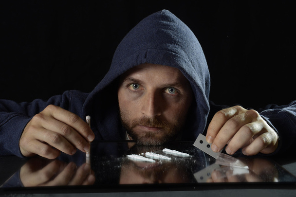 Young drug addict man on hood alone sniffing and snorting cocaine lines with rolled banknote on mirror - Photo, Image