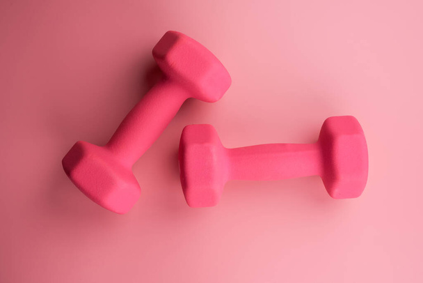 Two pink female dumbbells isolated on pink background close-up with copy space. Fitness concept, weight loss and sport activity, top view, flat lay - Fotó, kép