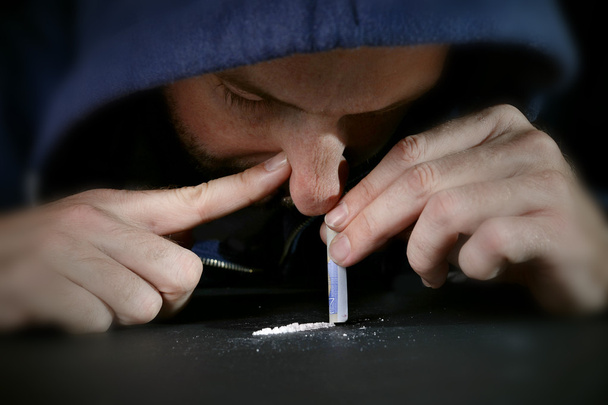 narkotyków nałogowiec człowieka na kaptur, parskanie linii kokainy z walcowanych banknotów - Zdjęcie, obraz