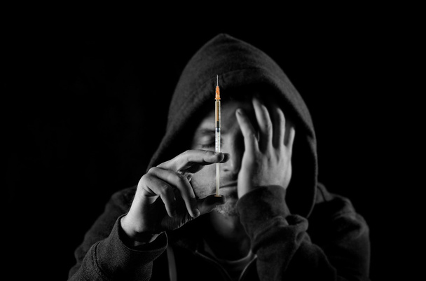 sick drug addict man wearing hood holding heroin or cocaine syringe - Photo, Image