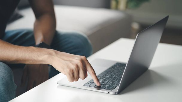 Молодий чоловік сидить на дивані вдома натисніть кнопку введення на клавіатурі ноутбука для онлайн роботи, використовуючи Інтернет, фрілансер, спокійний, сучасний спосіб життя, робота вдома
 - Фото, зображення