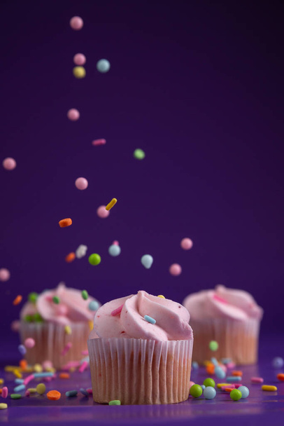 Sprinkles raining down on a pink mini cupcake - Photo, Image
