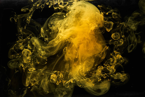 Abstract liquid art, yellow smoke bomb on black background, amber color acrylic paints under water - Foto, immagini