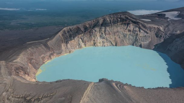 Niesamowite, martwe jezioro w kraterze wymarłego wulkanu. Strome skaliste zbocza. Na turkusowej wodzie widoczne są osady siarki. Widok z wysokości. Kamczatka - Zdjęcie, obraz