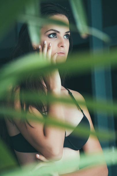 Photograph camouflaged in plants, hand to face, black bra, stare. - Photo, Image