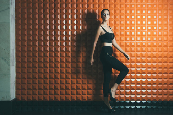 Fashion photography, fashion pose, orange background, checkered wall, hair up, black outfit,high heels. - Photo, Image