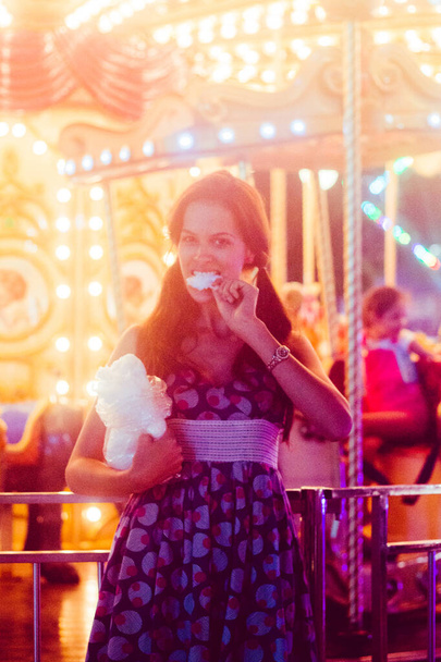 Photo in front of carousel, eat cotton candy, girl in dress, yellow light. - Photo, Image