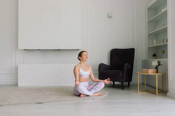 Health concept. Young beautiful woman does yoga exercise in a modern room - Photo, Image