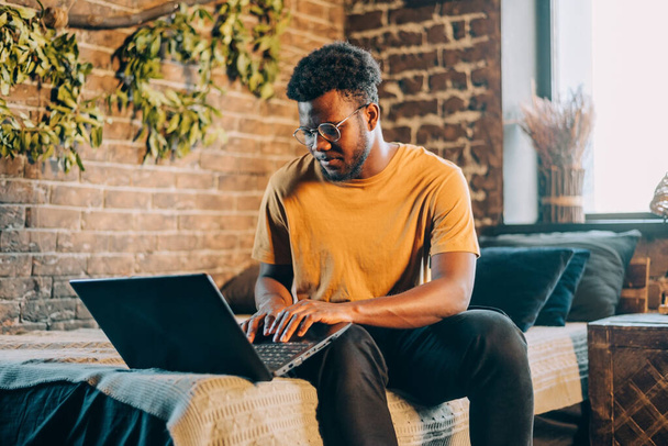 Young attractive black man working at home indoors with computer laptop. IT professions online - Photo, Image