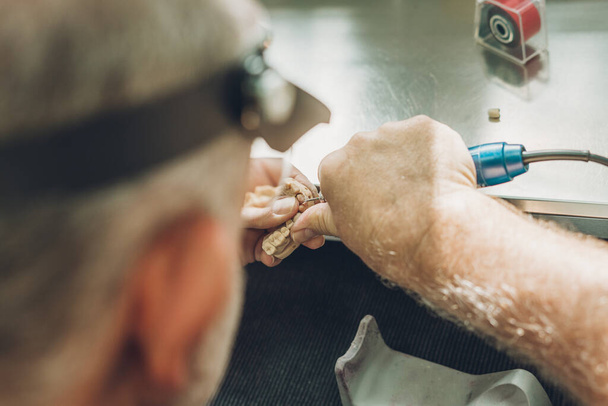 Vista ravvicinata delle mani di un uomo che regolano uno stampo dentale utilizzando un micromotore elettrico in un laboratorio dentale - Foto, immagini