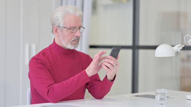 Yaşlı adam interneti iş yerinde akıllı telefondan tarıyor.  - Fotoğraf, Görsel