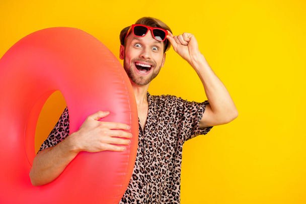 Photo of pretty excited young guy wear leopard outfit arm dark eyewear holding inflatable buoy empty space isolated yellow color background - Photo, Image
