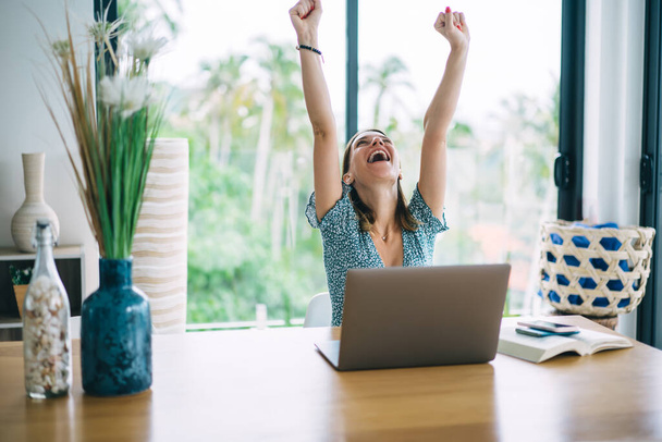 Emotional happy woman freelancer raising hand celebration achievement of successful online project, overjoyed 20 female accomplished educational course on laptop computer sitting in apartment - Фото, изображение