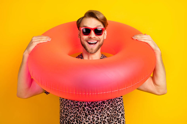Photo of cute funny young gentleman dressed print shirt dark glasses holding head swim circle isolated yellow color background - Foto, Bild