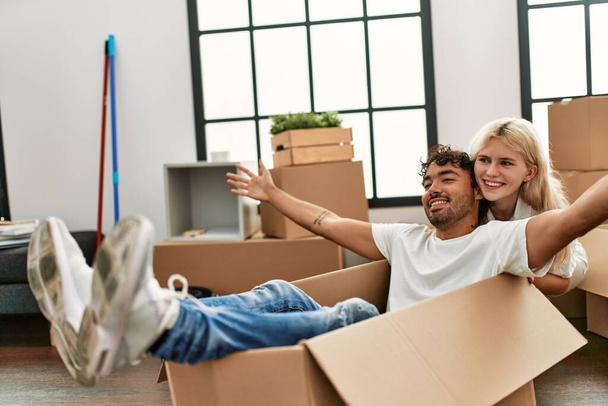 Молода красива пара посміхається щаслива гра з використанням картонної коробки як машини в новому будинку
. - Фото, зображення