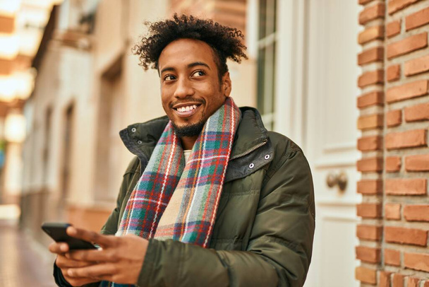 Junger Afroamerikaner lächelt glücklich mit Smartphone in die Stadt - Foto, Bild