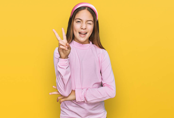 Gyönyörű barna kislány visel alkalmi garbó pulóver mosolyog boldog arc kacsintott a kamera csinál győzelem jele. Második..  - Fotó, kép