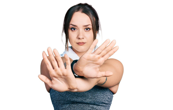 Молодая латиноамериканка в спортивной одежде и полотенце с неодобрительным выражением лица скрещивает руки, делает негативный знак, сердится на лицо  - Фото, изображение
