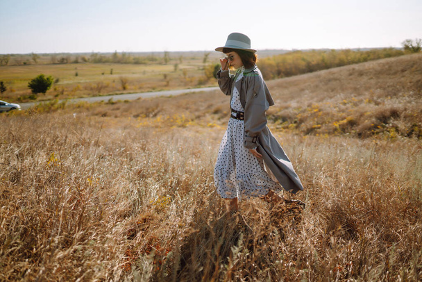 Stylish woman in coat and hat enjoys autumn nature. Young woman walks in the park, meadow. People, freedom, lifestyle, travel and vacations concept. - Valokuva, kuva