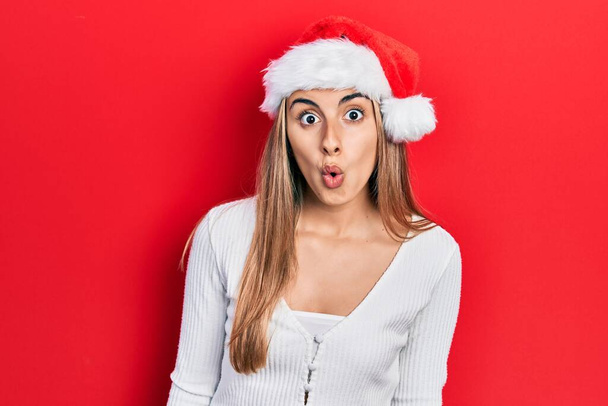 Mulher hispânica bonita usando chapéu de Natal com medo e chocado com expressão surpresa, medo e rosto animado.  - Foto, Imagem