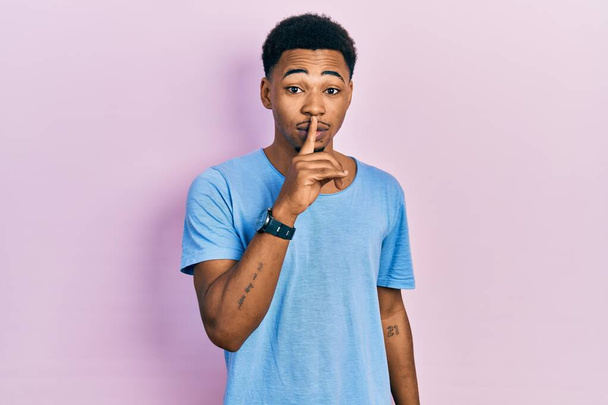 Jonge Afro-Amerikaanse man draagt een casual blauw t-shirt met de vraag om stil te zijn met de vinger op de lippen. stilte en geheim concept.  - Foto, afbeelding