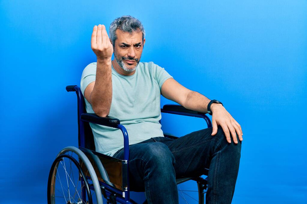Handsome middle age man with grey hair sitting on wheelchair doing italian gesture with hand and fingers confident expression  - Fotografie, Obrázek
