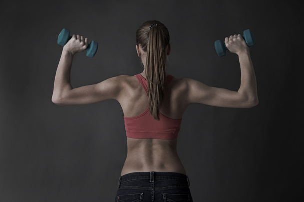 Young beautiful fitness girl exercising with dumbbells, on gray background - Φωτογραφία, εικόνα