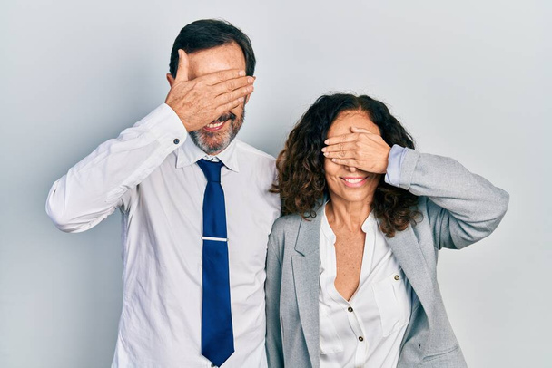 Middle age couple of hispanic woman and man wearing business office uniform smiling and laughing with hand on face covering eyes for surprise. blind concept.  - Foto, immagini