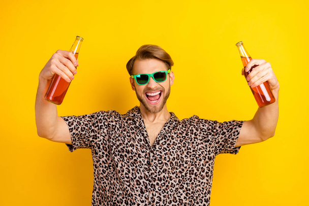 Photo of funky charming young guy wear leopard outfit dark eyewear drinking beer isolated yellow color background - 写真・画像