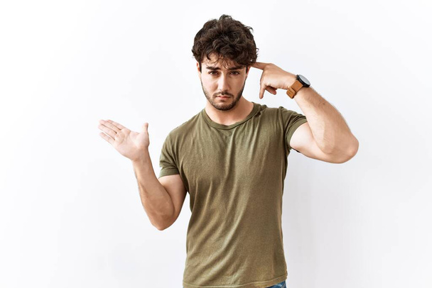 Hispanic man standing over isolated white background confused and annoyed with open palm showing copy space and pointing finger to forehead. think about it.  - Fotó, kép