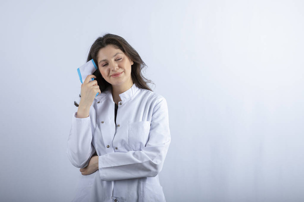Εικόνα της γυναίκας γιατρού με θερμόμετρο στέκεται σε λευκό φόντο. Υψηλής ποιότητας φωτογραφία - Φωτογραφία, εικόνα
