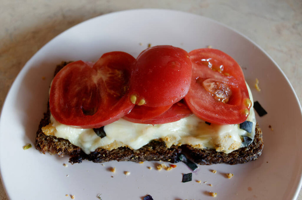 Rye bread sandwich with tomatoes, melted cheese, basil and chicken on a pink plate close-up - Photo, Image