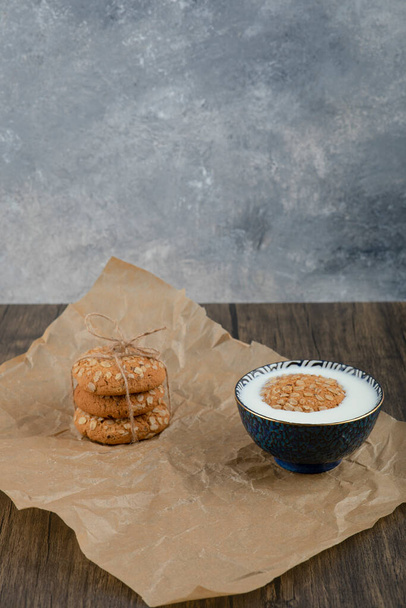 おいしいオートミールクッキーと木の表面に新鮮な牛乳のボウルのスタック。高品質の写真 - 写真・画像