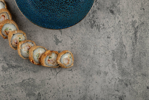 Piatto blu e gustosi rotoli di sushi caldo sulla superficie di pietra. Foto di alta qualità - Foto, immagini