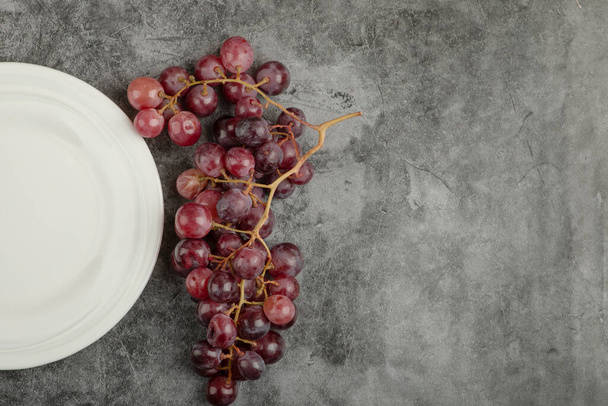Beyaz tabak ve mermer masada kırmızı lezzetli üzümler. Yüksek kalite fotoğraf - Fotoğraf, Görsel