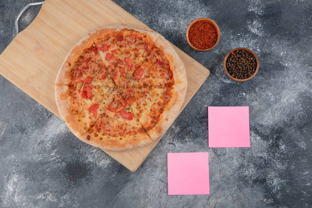 Deliciosa pizza cursi con condimentos y papeles sobre fondo de piedra. Foto de alta calidad - Foto, Imagen