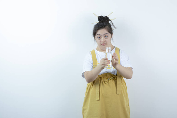 Junges hübsches Mädchen Modell steht und hält Glasflasche gegen weiße Wand. Hochwertiges Foto - Foto, Bild
