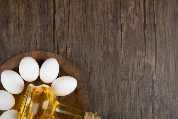 Ovos brancos crus e garrafa de azeite em tábua de madeira. Foto de alta qualidade - Foto, Imagem