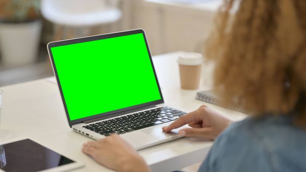 Vista trasera de la mujer africana usando el ordenador portátil con la pantalla dominante verde del croma  - Foto, Imagen
