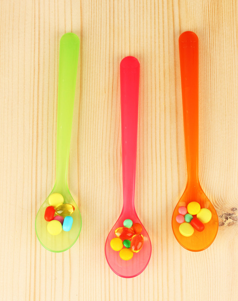 Plastic spoons with color pills on wooden background - Foto, imagen